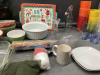TOTE W/ MISC HOUSEHOLD ITEMS - ACRYLIC CUPS, BOWLS, (2) SQUARE CAKE PANS, (4) SMALL CORELLE PLATES, BLUE GLASSES ETC - 3